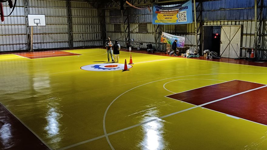Gimnasio con piso amarillo y rojo recién terminado, con líneas de básquetbol