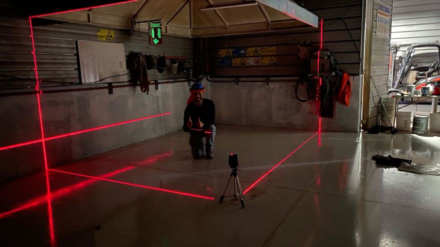 Operario con un nivel láser proyectando líneas rojas sobre el piso de un taller