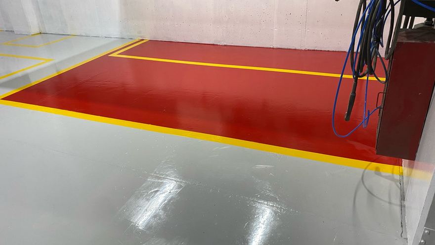 Zona de trabajo roja con borde amarillo sobre piso gris brillante